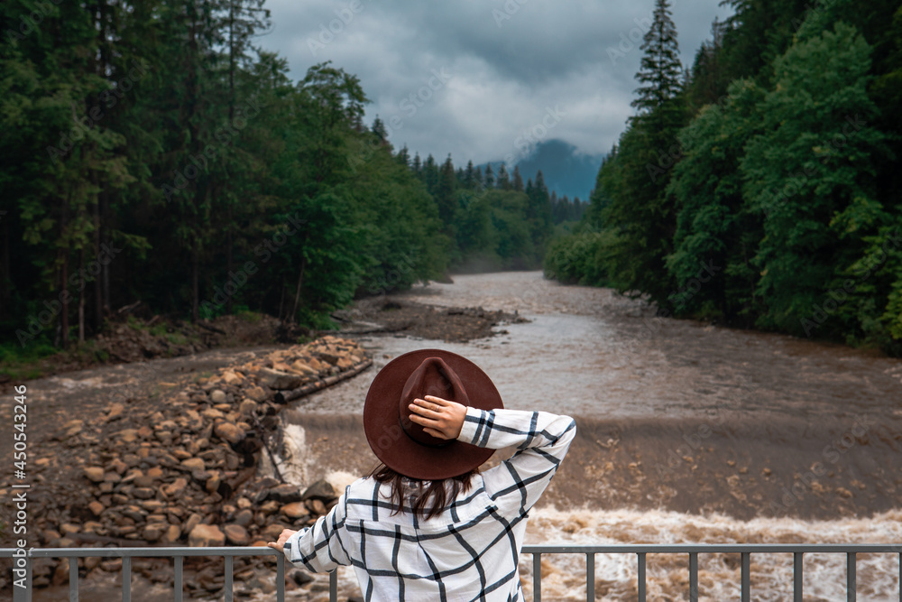 woman in brown hat looking at mountain river after storm