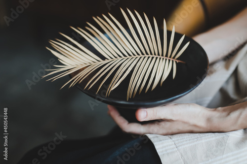 female hands holding a black ceramic plate decorated with fern leaf close-up