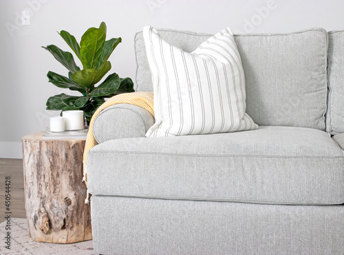 A modern farmhouse home decor scene with couch, wood stump end table, throw pillows and fiddle leaf fig houseplant.