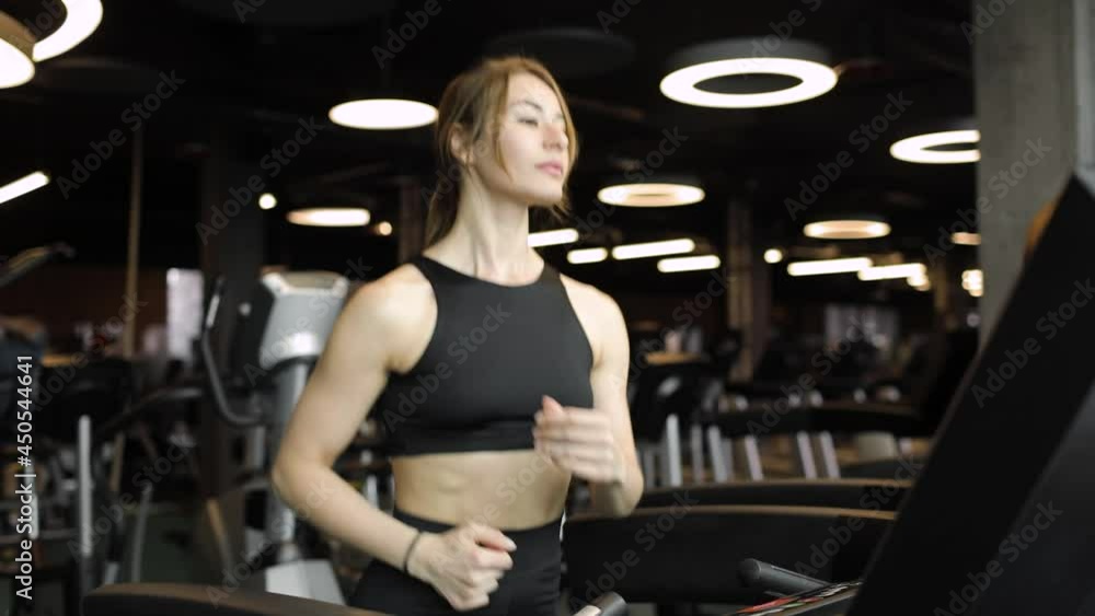 Young athletic woman in a short black tank top does cardio exercise on modern treadmill in sport club. Sport. The concept of an active and healthy lifestyle. Young athletic woman in a short black tank top does cardio exercise on modern treadmill in sport club. Sport. The concept of an active and healthy lifestyle.