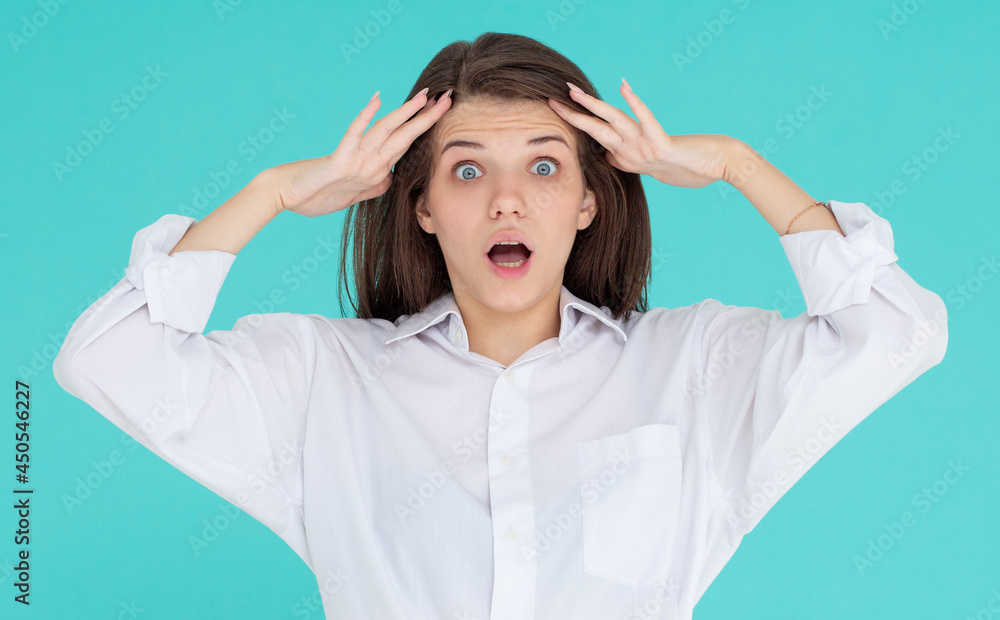 Shocked amazed young woman with hands on head standing and shouting over blue background Shocked amazed young woman with hands on head standing and shouting over blue background