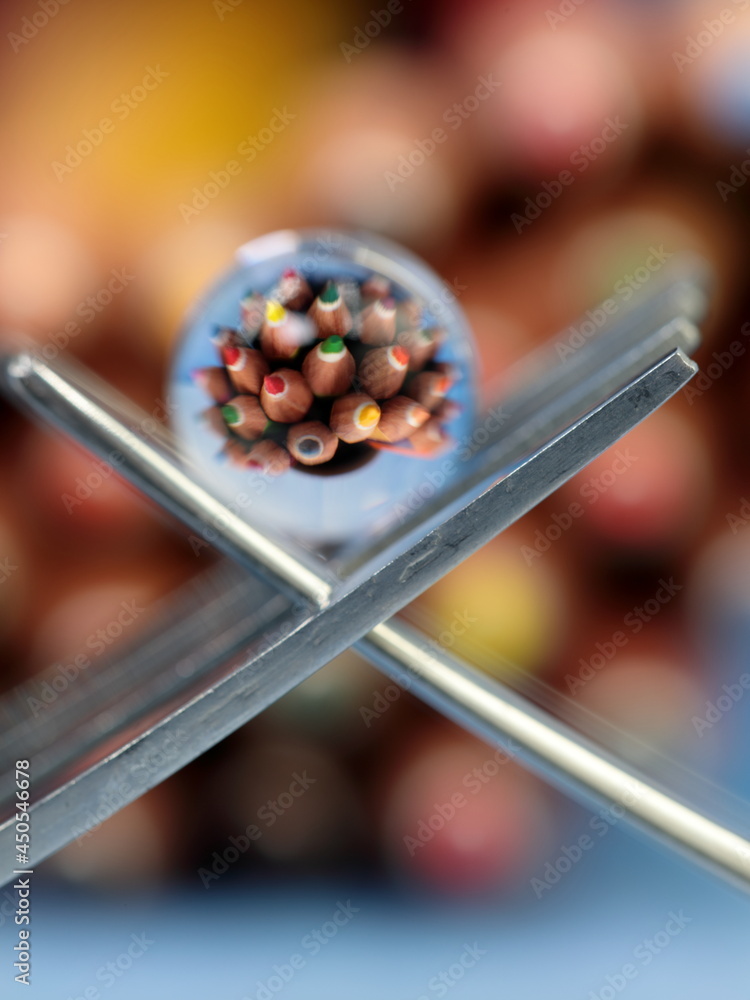 A still life of small transparent balls on forks with a reflection of colored pencils.