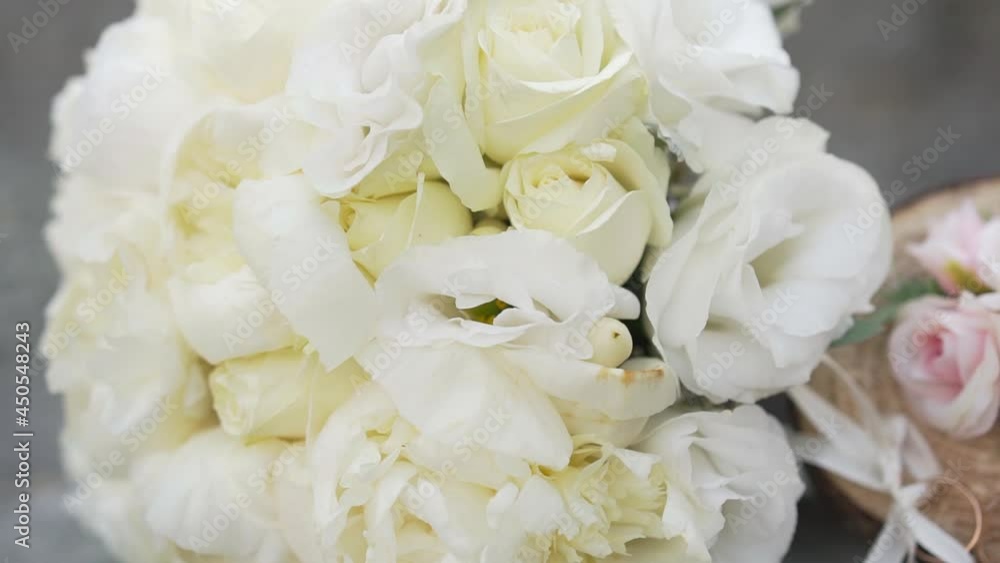 Beautiful lush wedding bouquet of fresh flowers with white roses and eustoma near jewelry. Next to it are two gold wedding rings tied with white satin ribbons to a wooden bar Beautiful lush wedding bouquet of fresh flowers with white roses and eustoma near jewelry. Next to it are two gold wedding rings tied with white satin ribbons to a wooden bar