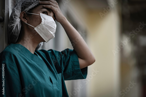 Tired depressed female asian scrub nurse wears face mask blue uniform sits on hospital floor,Young woman doctor stressed from hard work