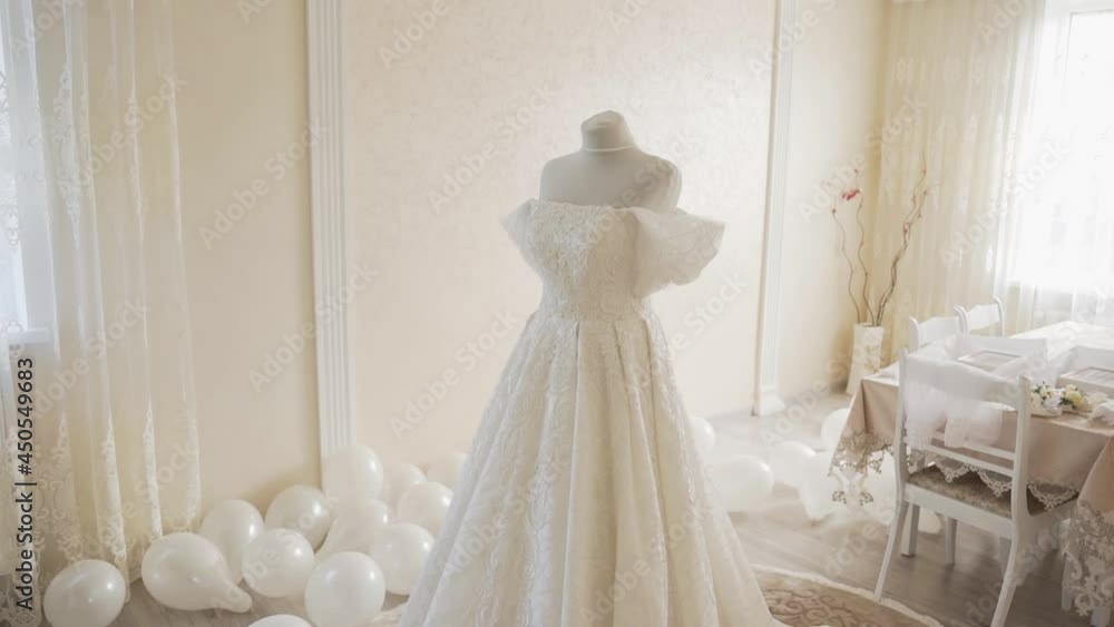 Luxurious lush wedding dress on a mannequin in the room. Clothes for bride. Expensive wedding dress made of beautiful fabric. Wedding dress with ruffled sleeves and sewn lace on the corset and skirt Luxurious lush wedding dress on a mannequin in the room. Clothes for bride. Expensive wedding dress made of beautiful fabric. Wedding dress with ruffled sleeves and sewn lace on the corset and skirt