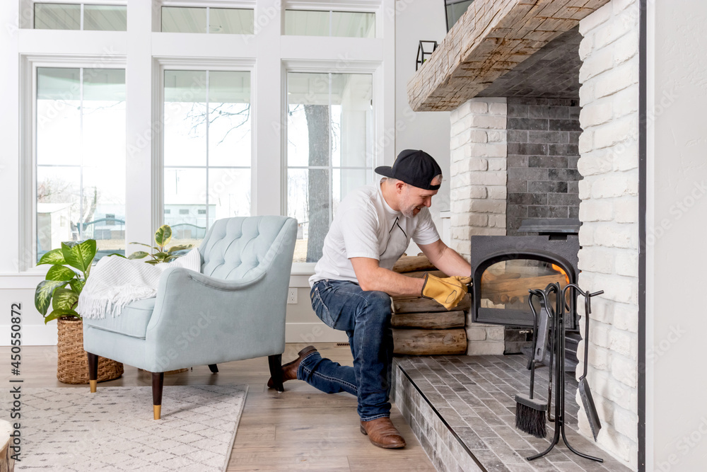An adult male in his 40s loading firewood into a wood burning stove in a modern farmhouse family room.