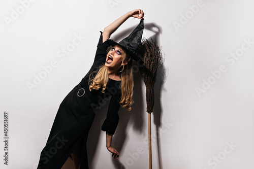 Enthusiastic curly girl enjoying carnival. Excited witch in black dress posing in halloween.