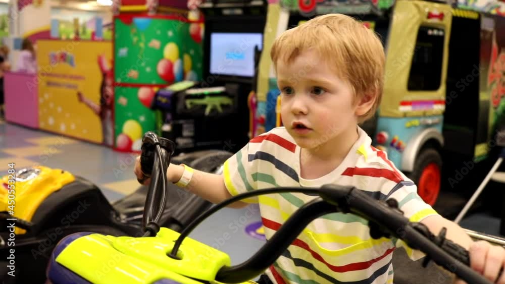 Little surprised happy boy playing driving game on motorcycle slot machine in amusement park. Children activity. Urban family lifestyle. True feelings. Emotional male child riding a lot. Little surprised happy boy playing driving game on motorcycle slot machine in amusement park. Children activity. Urban family lifestyle. True feelings. Emotional male child riding a lot.