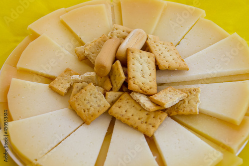 Delicioso plato de queso de oveja con palitos de pan españoles listos para comer. Plato de queso bellamente presentado sobre un mantel amarillo. photo