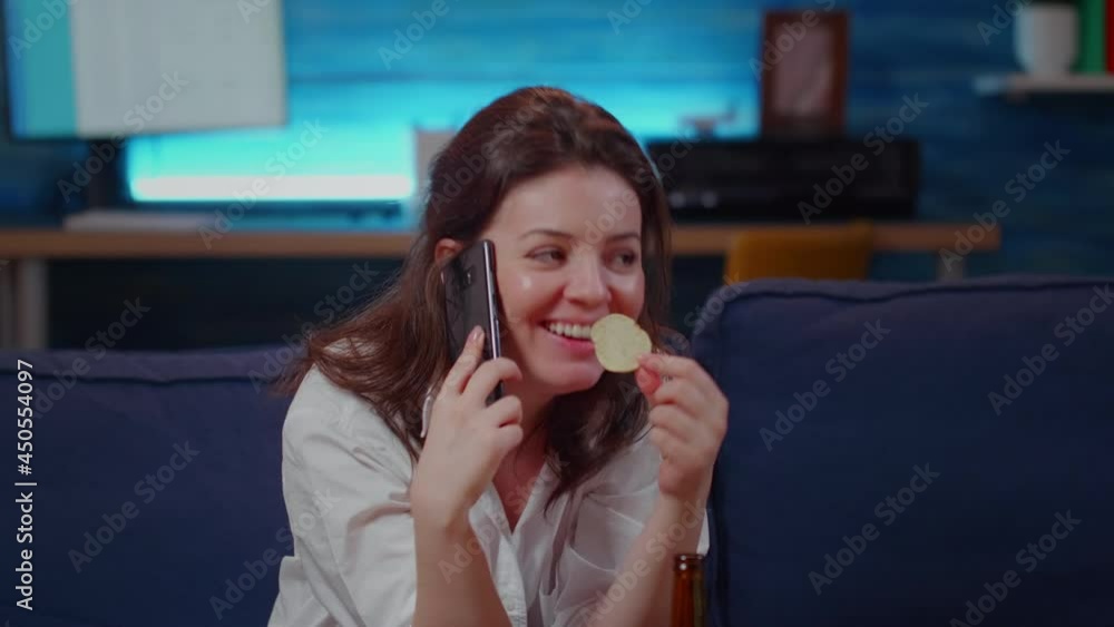 Person talking on phone call with friend in living room while eating chips and relaxing. Caucasian woman having fun conversation on smartphone, sitting on couch with snack after work Person talking on phone call with friend in living room while eating chips and relaxing. Caucasian woman having fun conversation on smartphone, sitting on couch with snack after work