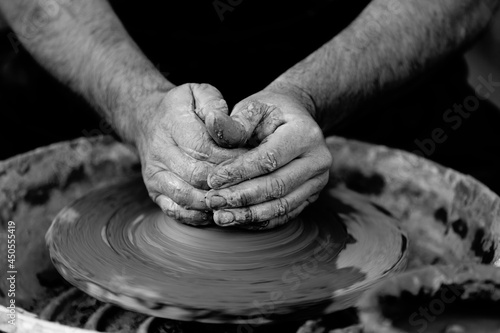 Black and white photo of potter molding clay with his hands on a spinning pottery wheel. Original public domain image from Wikimedia Commons photo