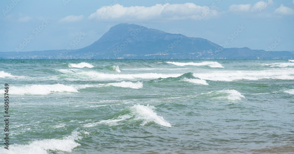 Rolling high ocean waves with view to the mountain of Denia, taken from Daimus, Spain Rolling high ocean waves with view to the mountain of Denia, taken from Daimus, Spain