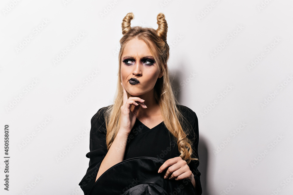 Pensive evil witch posing on white background. Halloween portrait of curious blonde girl. Pensive evil witch posing on white background. Halloween portrait of curious blonde girl.