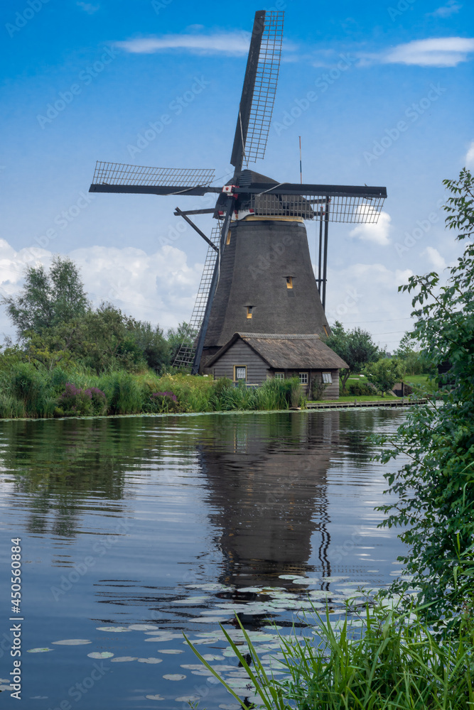 Vertical Dutch landscape with traditional windmill, water canal, and little cottage. Postcard view from Kinderdijk, Netherlands 