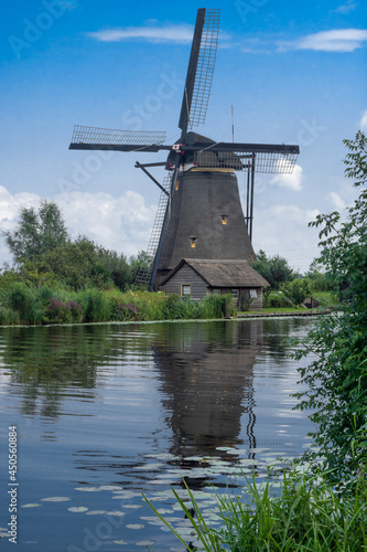 Obraz na płótnie Vertical Dutch landscape with traditional windmill, water canal, and little cottage. Postcard view from Kinderdijk, Netherlands w salonie