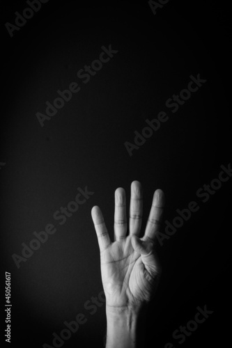 Black and white image of hand demonstrating sign language number four against black background with empty copy space