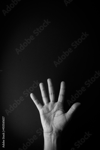 Black and white image of hand demonstrating sign language number five against black background with empty copy space