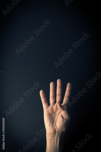 Colour image of hand demonstrating sign language number four against dark background with empty copy space