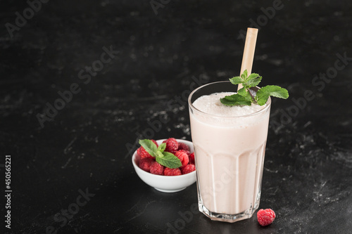Lassi drink with raspberries in a glass with mint and a bamboo tube on a dark background.