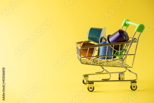 A food basket full of colorful aluminum coffee capsules on a yellow background. Side view, copy space