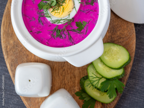 Close-up of cold chlodnik soup on a wooden board. Soup of Polish Belarusian and Russian cuisine made of beetroot and kefir, decorated with half an egg. Healthy food. Top view, flat lay photo