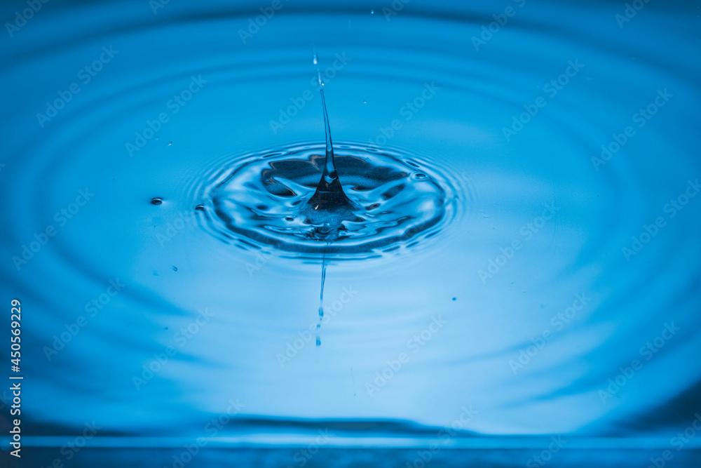 Close up view of drops making circles on blue water surface isolated on background.