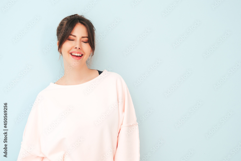 Portrait of young beautiful smiling female in trendy summer pink clothes. Sexy carefree woman sitting near light blue wall in studio. Positive model having fun indoors. Cheerful and happy Portrait of young beautiful smiling female in trendy summer pink clothes. Sexy carefree woman sitting near light blue wall in studio. Positive model having fun indoors. Cheerful and happy