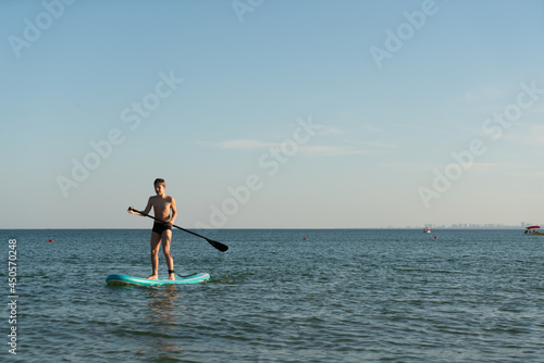 A 12 year old boy learns to stand on a SUP board in the sea near the shore. © Виктор Кеталь