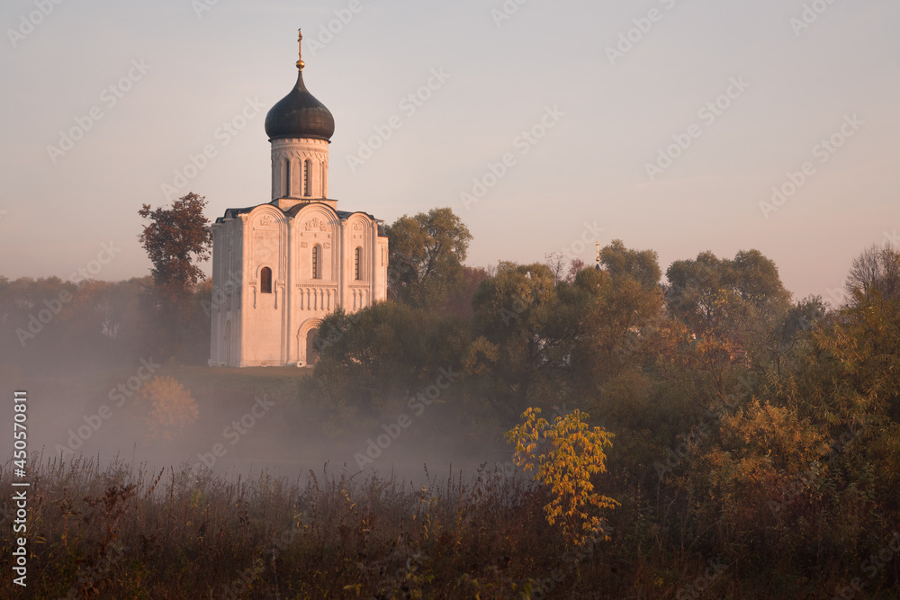 Old Russian Orthodox church lit by the rising sun above autumn forest in a light mist