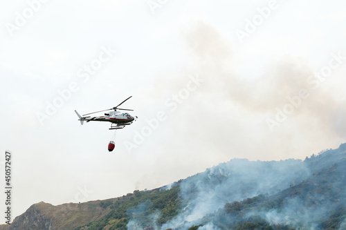 Fire helicopter dropping water from a bucket on a forest fire in the mountains. Forest fire is an environmental disaster. Deforestation.