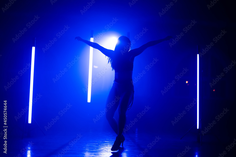 Woman in sexy outfit with heels sensually dancing in dark studio with blue lamps. Creative lady actively moving to music. Concept of choreography, dance, performance. Woman in sexy outfit with heels sensually dancing in dark studio with blue lamps. Creative lady actively moving to music. Concept of choreography, dance, performance.