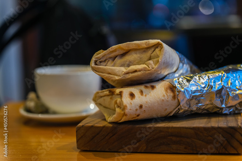 Two shawarma, a donner kebaba, wrapped in foil, lie on a thick wooden stand. photo