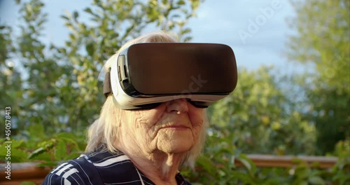 open-minded grandma turning her head in virtual reality glasses and looking at the camera smiling. pensioner raises her head to the sky in a viar helmet. positive attitude of the older generation to photo