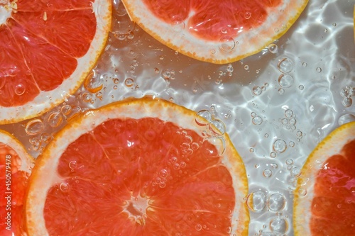 Close up view of the red grapefruit slices in lemonade background. Texture of cooling sweet summer's drink with macro bubbles on the glass wall. Flat design