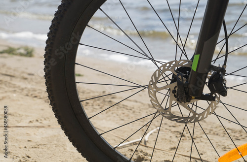 Front wheel of a bicycle, in the background river sand and waves