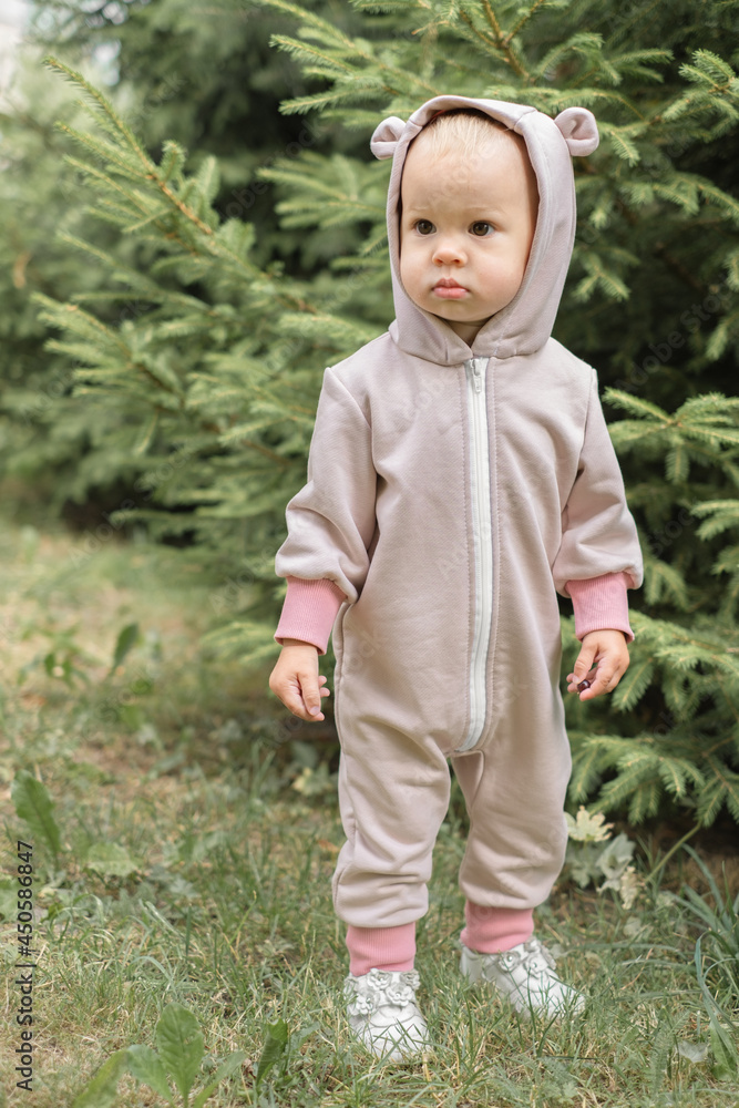 A serious kid stands near a tree and looks away.