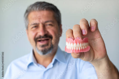 Bild auf Leinwand An old gray-haired man holds his denture