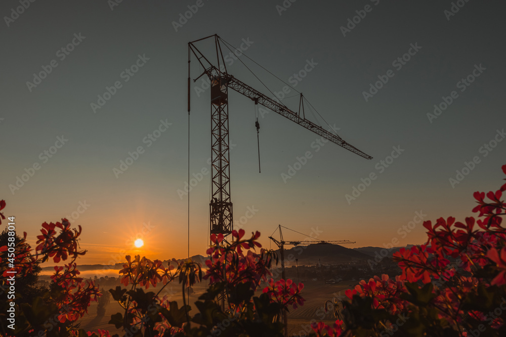 Naklejka premium Construction site of an apartment building in early morning with sunrise, visible mist and fog on the fields. Epic modern photo of construction site.