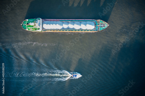 Top down aerial shot of the tanker loaded by stacks of sand and speedboat is sailing through