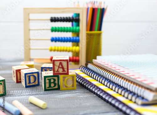 Wooden alphabet blocks on a white wooden background. Back to school, games for kindergarten, preschool education. Abacus, pencils, notebooks, blocks on the table.