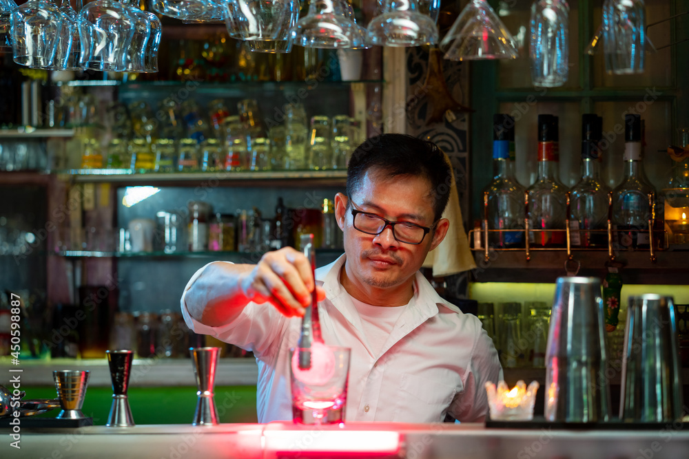 Bartender preparing tasty mixed alcoholic drink with ice cube in decorated cocktail glass on bar counter for customer in nightclub. Celebration party, nightlife business and alcohol addiction concept
