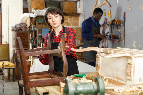 Portrait of female furniture restorer inspecting antique armchair for restoration in workshop © JackF
