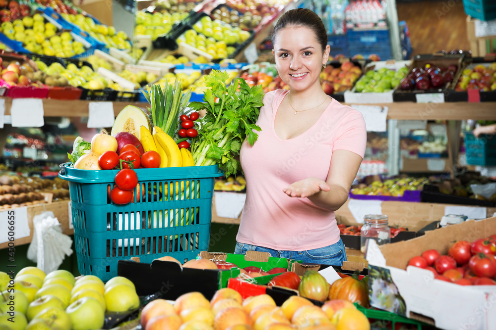 Young satisfied woman with basket filled with fresh fruits and vegetables at the store