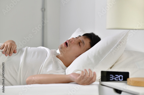 Young Asian man sleeping and snoring loudly lying in the bed. photo