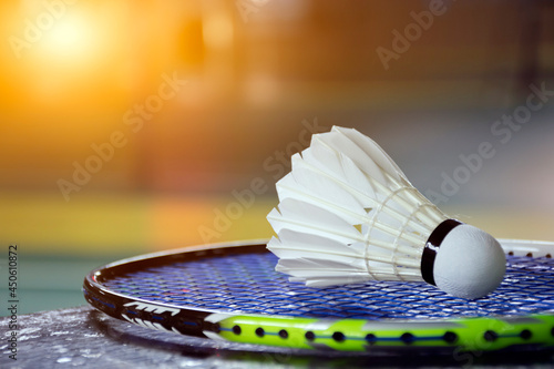 Cream white badminton shuttlecock and racket with neon light shading on green floor in indoor badminton court, blurred badminton  background, copy space. © Sophon_Nawit