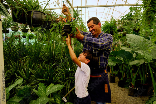 cheerful latinx Mexican middle aged father and young children son gardener working together in a greenhouse