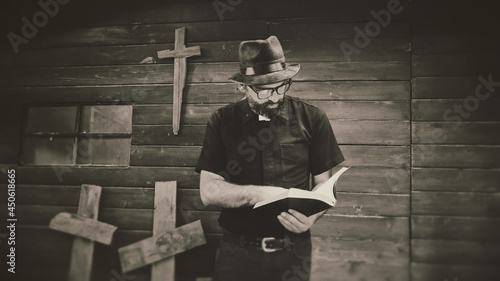 Clergyman, reverend or priest wearing a clerical collar and reading a bible. Preacher preaching the gospel in front of an old rustic rural church. photo