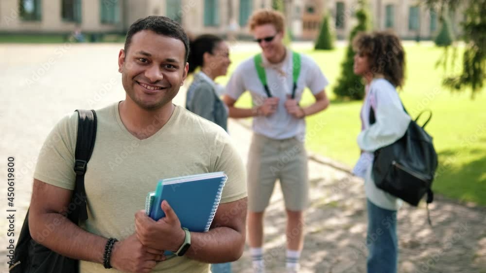A smiling american student is looking to the camera standing on campus outside A smiling american student is looking to the camera standing on campus outside