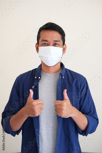 Adult Asian man giving two thumbs up while wearing protective medical mask photo