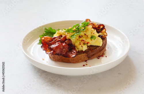 Rye bread toast with scrambled eggs and fried bacon close up